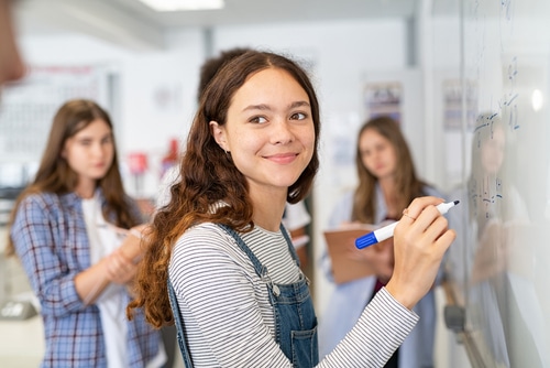 A young woman smiling while standing at a whiteboard.