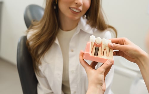A woman holds a tooth model in her hand, demonstrating dental education or oral health awareness.