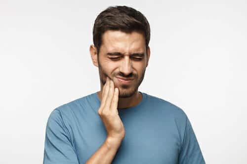 A man holding his face from tooth pain which may require a tooth extraction in Grove City, OH