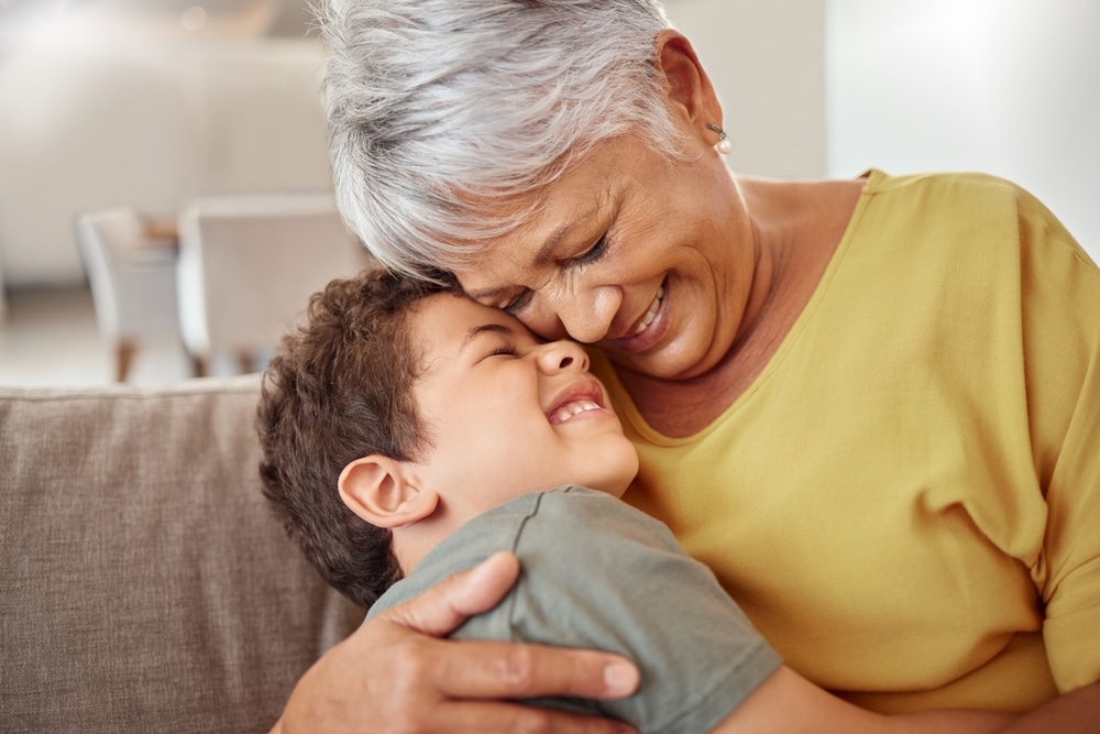 An elderly person and a child smiling and hugging indoors.
