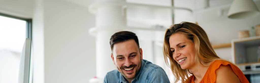 A couple smiling in a cafe, looking at something together.