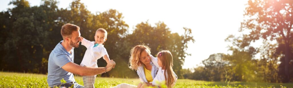 A family enjoys a sunny day, sitting together on the grass in a lush green field, surrounded by nature.