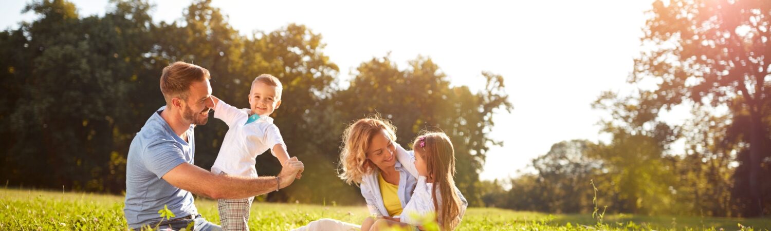 A family enjoys a sunny day, sitting together on the grass in a lush green field, surrounded by nature.