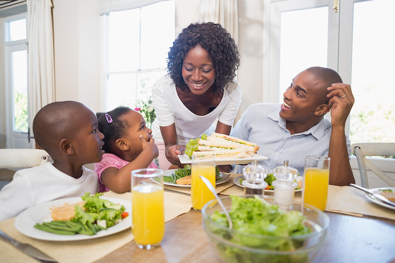 A family gathered around a table enjoying sandwiches and salad during a meal together.
