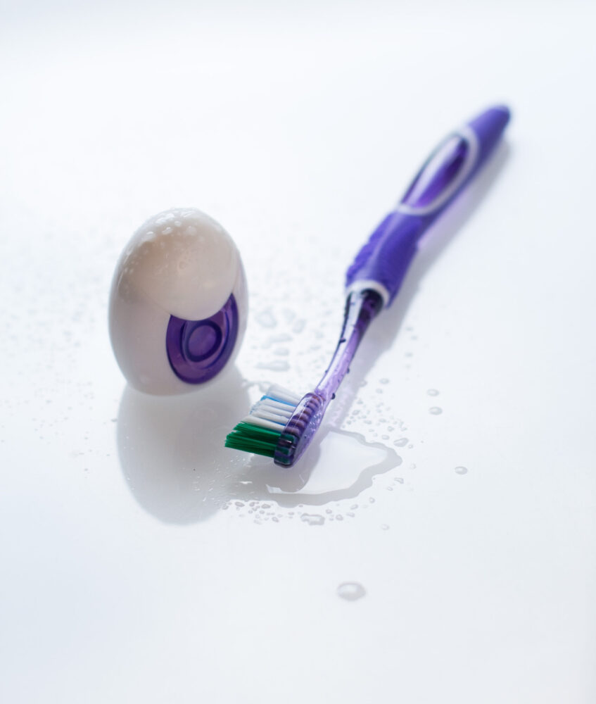 A purple toothbrush and oval soap container on a wet, glossy white surface.